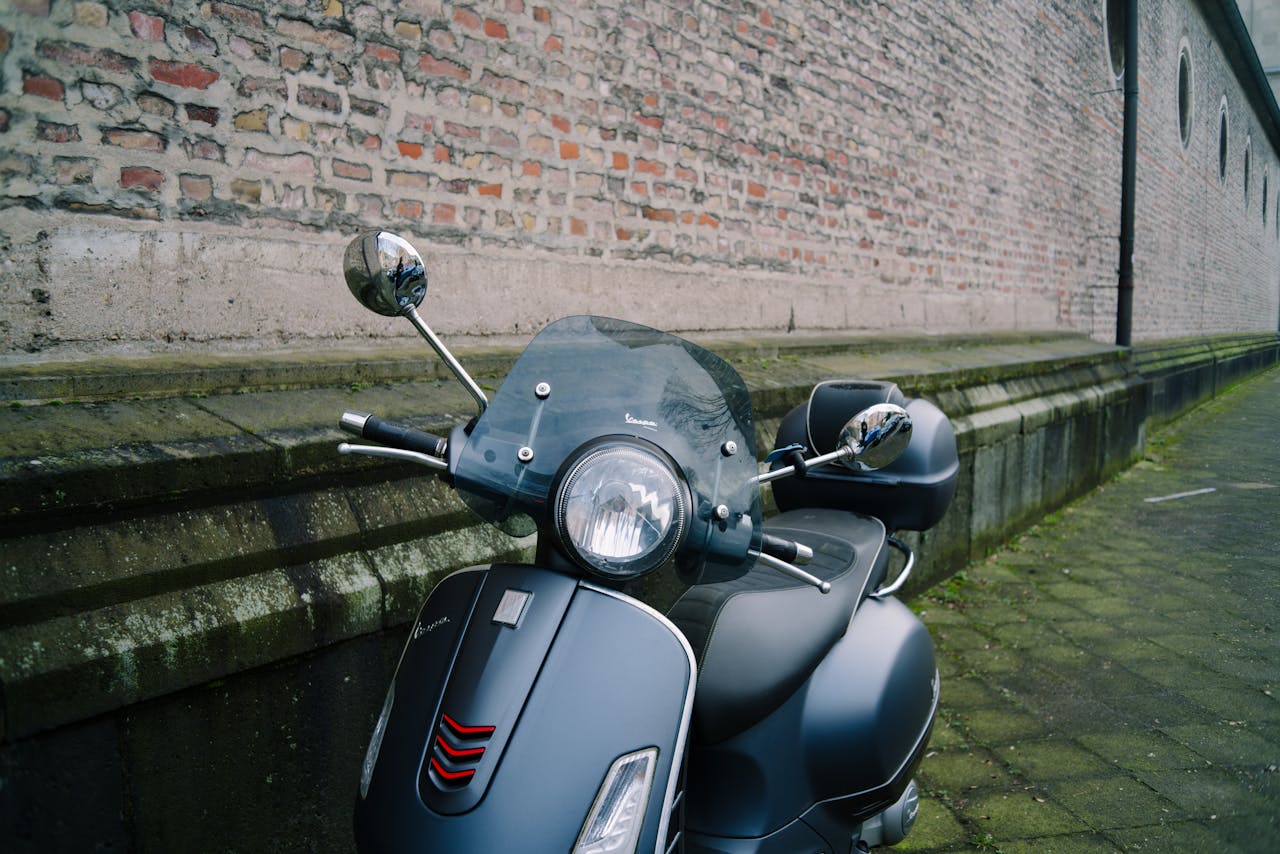 Close-up of a classic Vespa scooter parked against a historic brick wall.